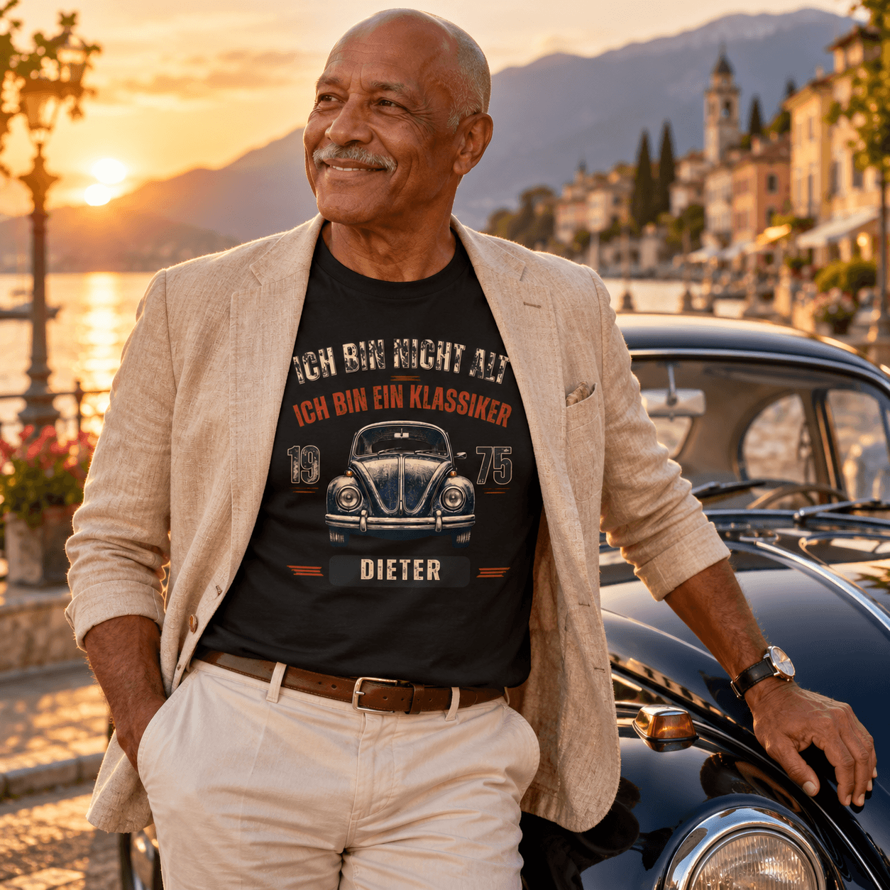 Lächelnder Mann an einem Oldtimer im T-Shirt mit Aufdruck: „Ich bin nicht alt, ich bin ein Klassiker – 1975 – Dieter“ und VW-Käfer-Motiv