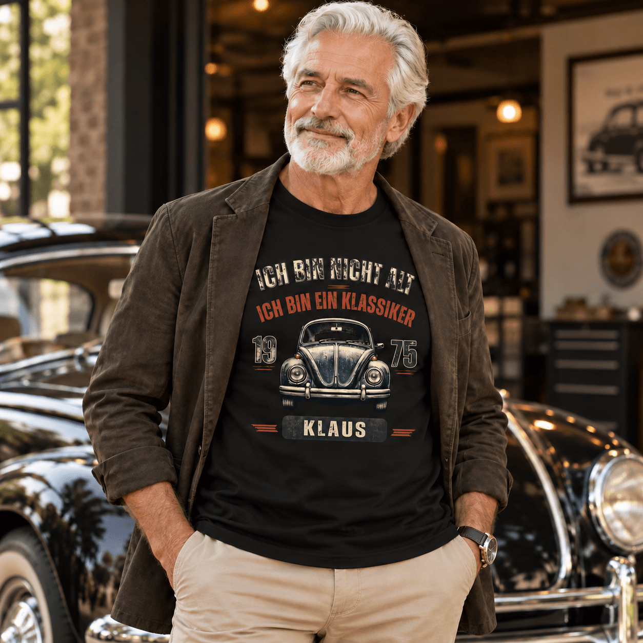 Älterer Mann vor einem Oldtimer im schwarzen T-Shirt mit Aufdruck: „Ich bin nicht alt, ich bin ein Klassiker – 1975 – Klaus“