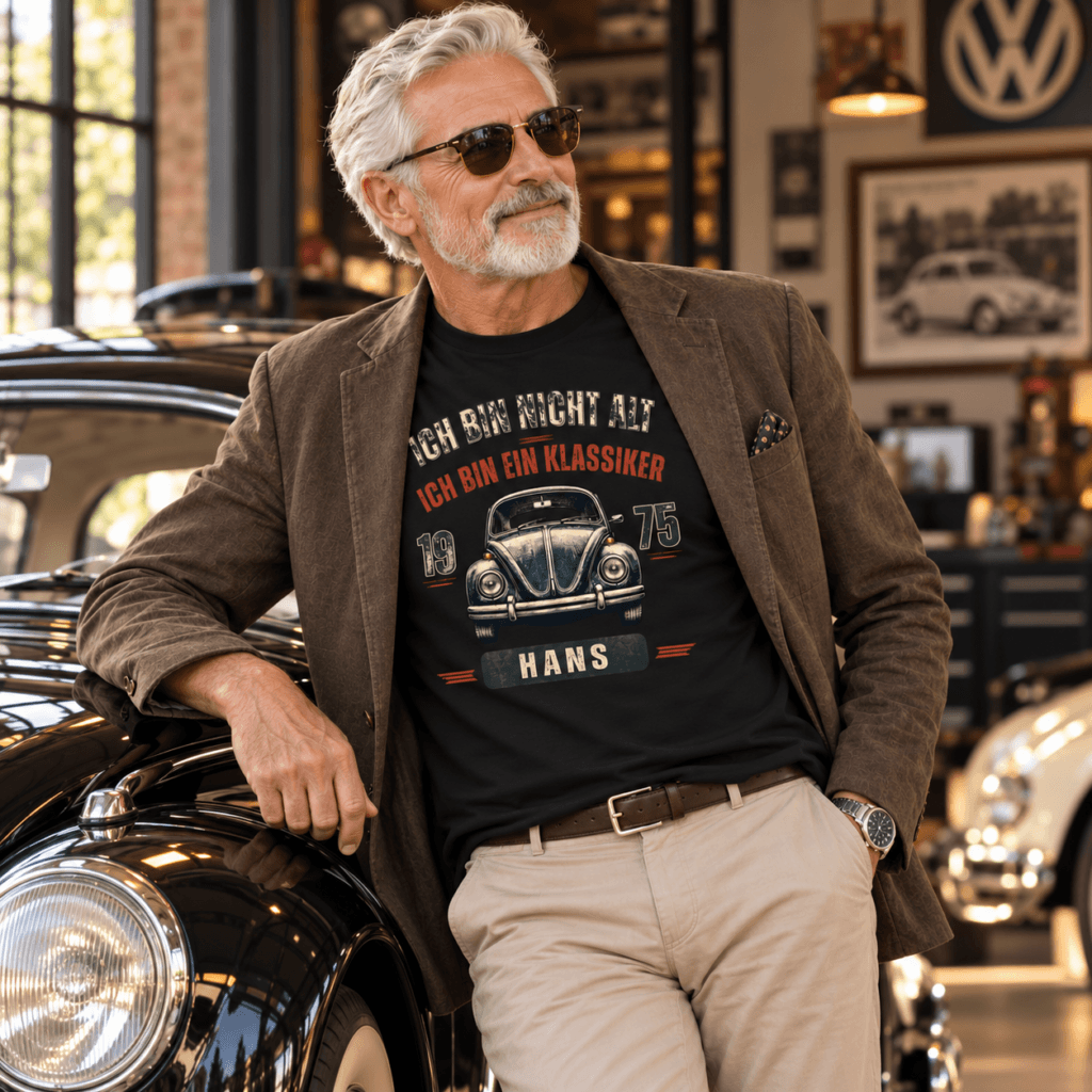 Mann an einem Oldtimer mit T-Shirt-Aufdruck: „Ich bin nicht alt, ich bin ein Klassiker 1975 Hans“ mit VW-Käfer